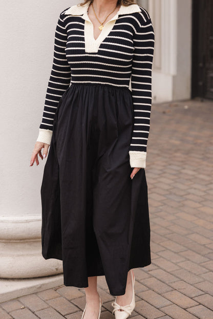 A woman stands outside in the Adelina Dress in Black by Ivy City Co, featuring a striped knit bodice, long sleeves, and a collared neckline. She wears cream shoes with bows; her face is not visible.
