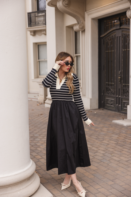 A woman stands by a white column in front of an ornate building, wearing sunglasses and the Ivy City Co Adelina Dress in Black.