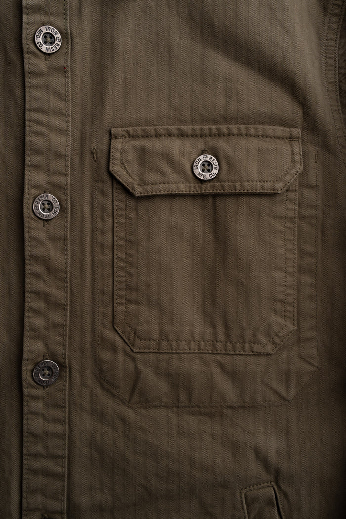 Close-up of a brown jacket with a buttoned flap pocket. Buttons are engraved with "Iron and Resin MFG. CO" for a rugged look.