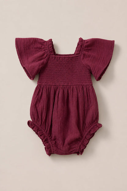 The Ivy City Co Baby Lennon Romper in Wildberry, featuring flutter sleeves, a smocked bodice, and ruffled leg openings, is laid flat on a neutral background.