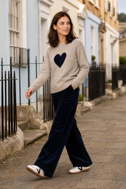 Model wearing the Aspiga Cashmere Crew Neck Heart Jumper in Oat/Navy with navy corduroy trousers, walking outdoors on a street