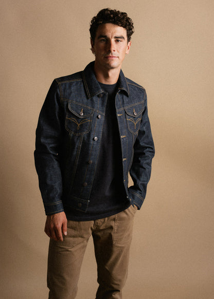 Man in a denim jacket and khaki pants stands against a beige background, exuding a casual and confident style.