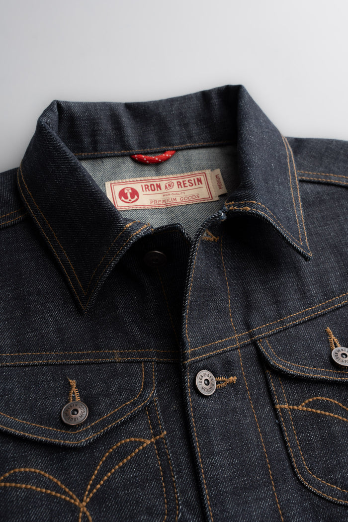 Denim jacket close-up with Iron and Resin label, showcasing detailed stitching and metal buttons on a textured fabric surface.