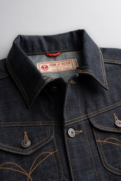 Denim jacket close-up with Iron and Resin label, showcasing detailed stitching and metal buttons on a textured fabric surface.