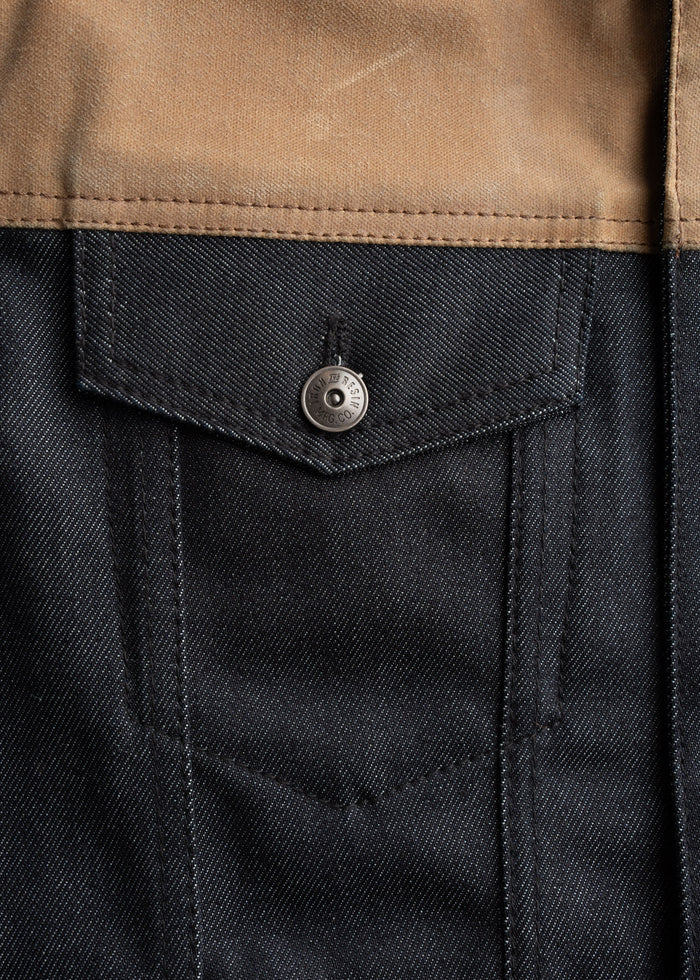 Close-up of a denim jacket pocket with a metal button and brown fabric detail, showcasing texture and stitching.