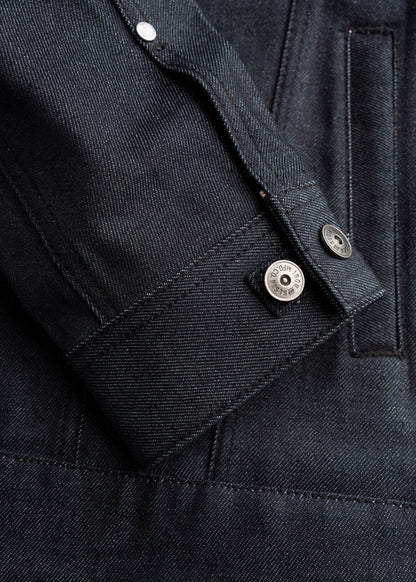 Close-up of a dark denim jacket sleeve with visible stitching and metal button details, showcasing texture and craftsmanship.