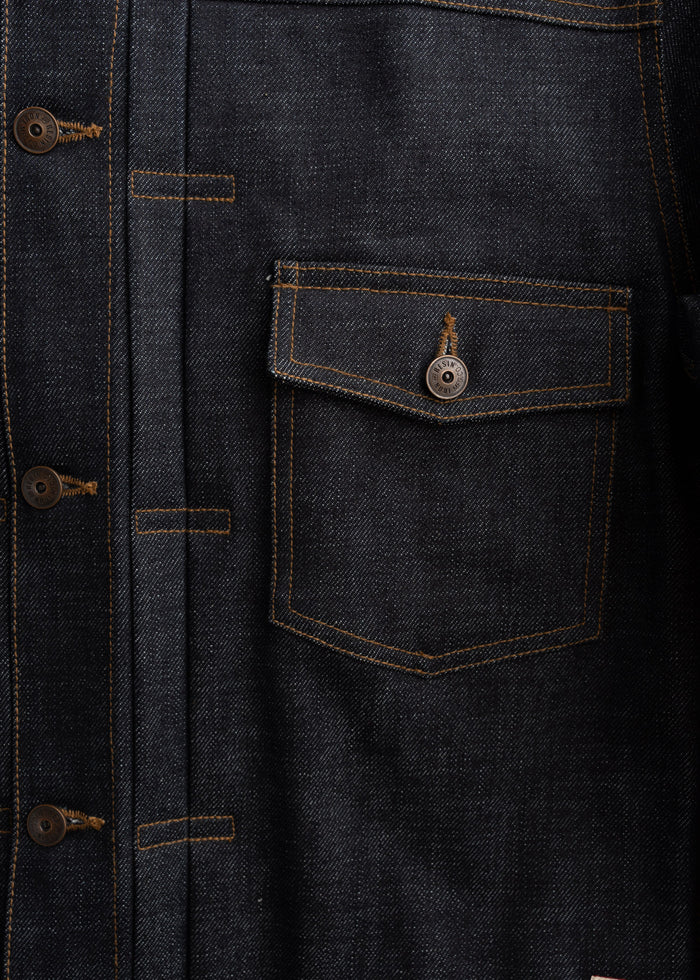 Close-up of a dark denim jacket with brown buttons and a buttoned pocket, showcasing detailed stitching and texture.