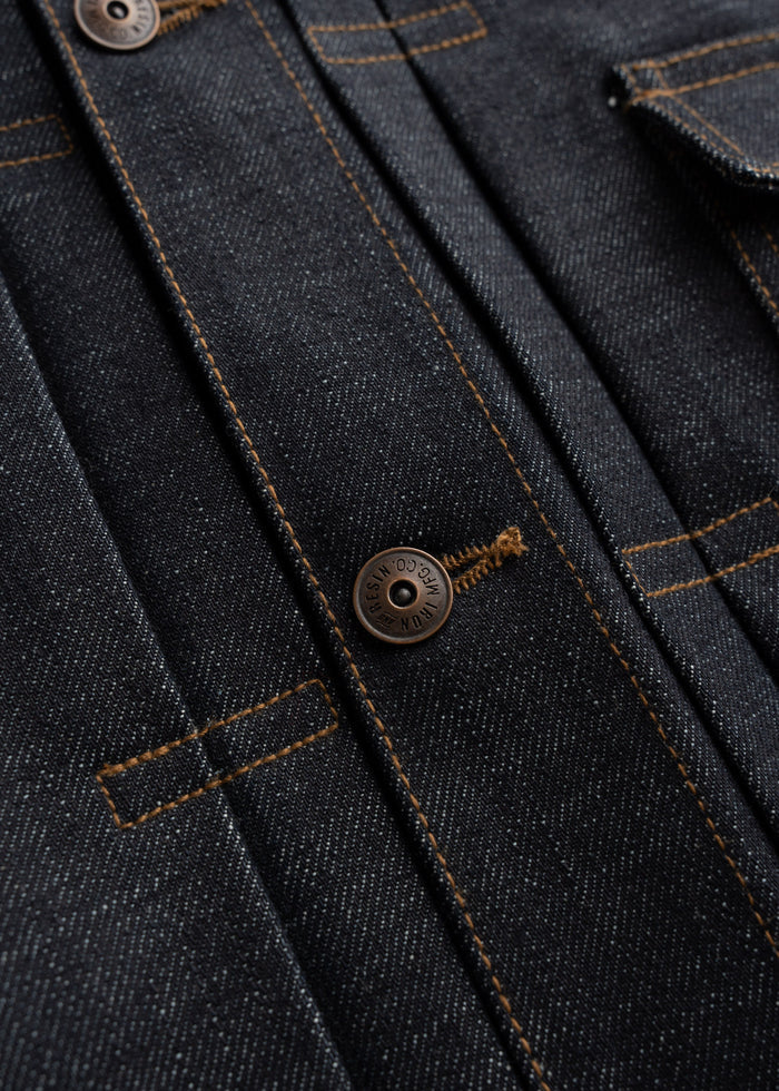 Close-up of a dark denim jacket with visible stitching and a metal button, showcasing texture and craftsmanship.