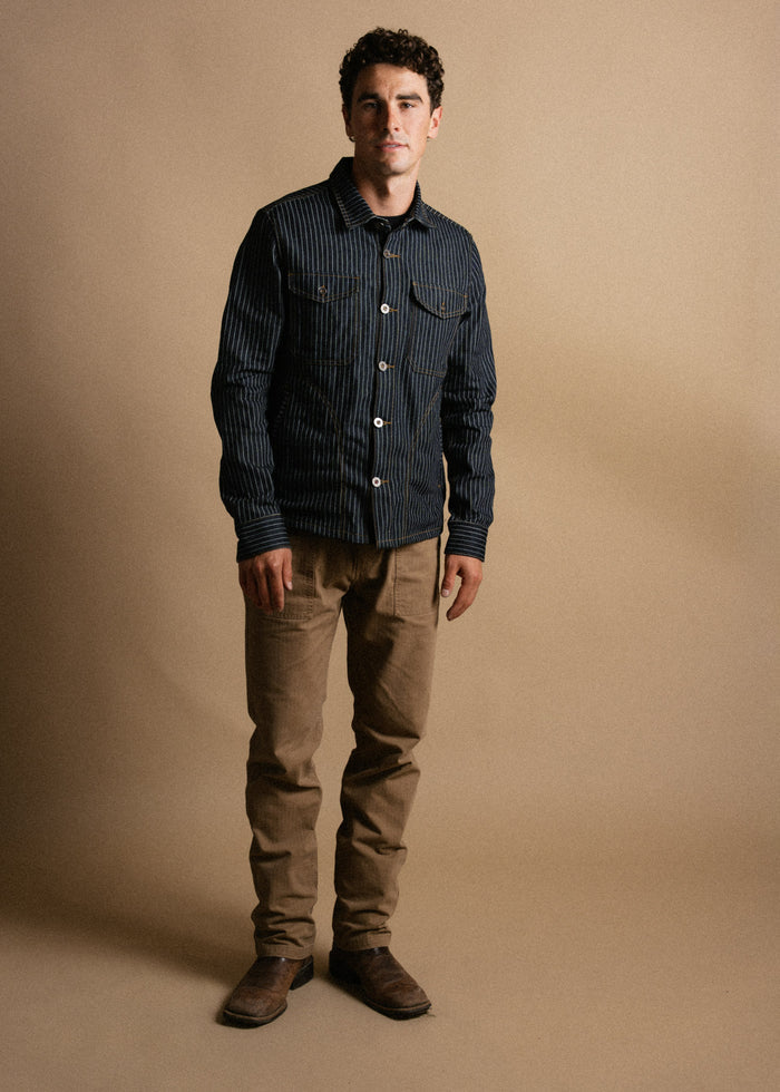 Man in a striped jacket and khaki pants stands against a beige background, exuding a casual yet stylish vibe.