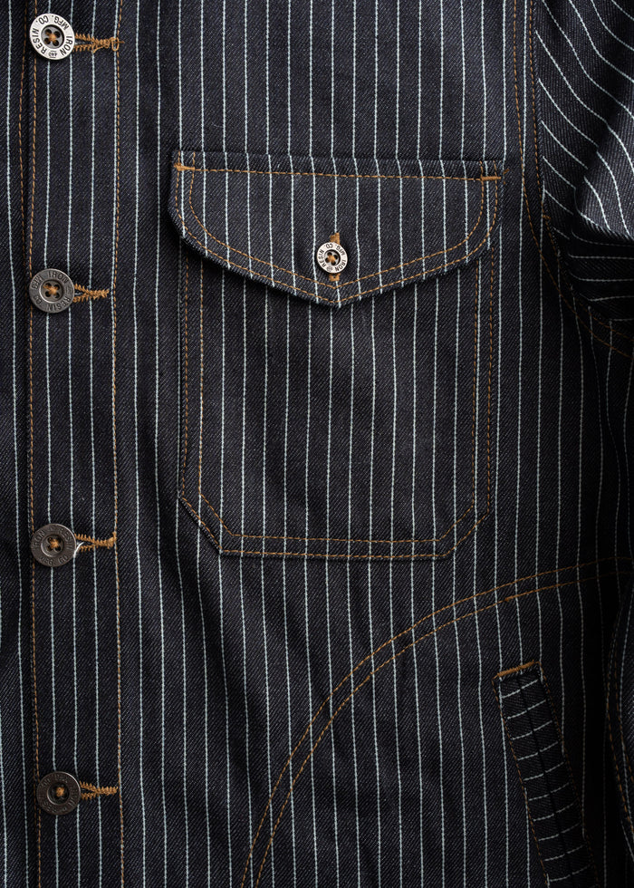 Close-up of a pinstripe denim jacket with brown stitching, featuring a buttoned pocket and visible buttons on the front.