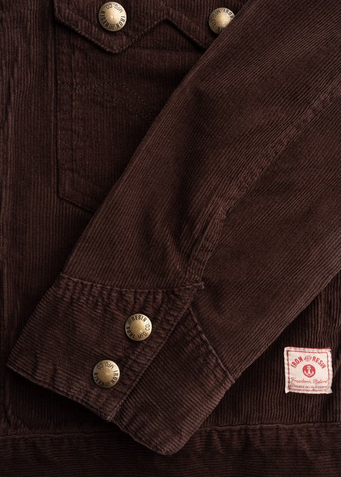 Brown corduroy jacket with brass buttons and "Iron and Resin" label. Close-up of sleeve and pocket detail.