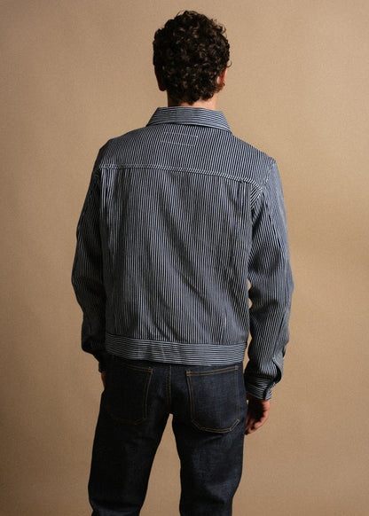 Man in striped jacket and jeans, facing away against a beige background. The casual outfit highlights a relaxed, stylish look.