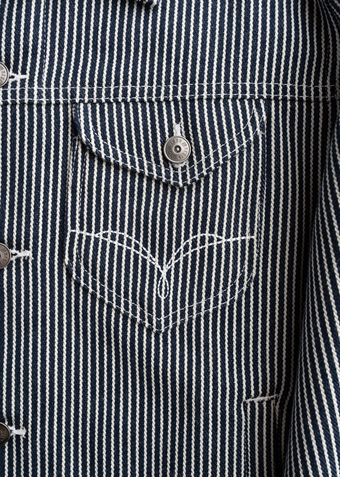Close up of chest pockets with button closure on denim jacket, showcasing stitching and utility design
