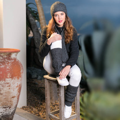 Woman sitting outside wearing grey Koru cable leg warmers.