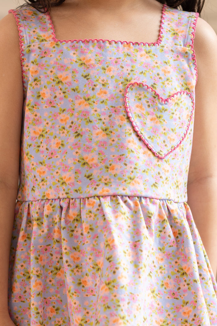 A child wears Ivy City Co’s Mini Blair Play Set in Vibrant English Garden—a sleeveless floral stretch dress with a pink-outlined heart pocket, square neckline, and gathered skirt for playful charm.