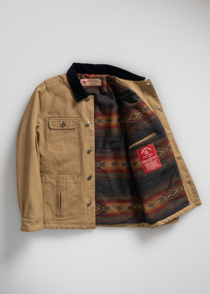 Tan jacket with black collar, open to reveal colorful patterned lining and red label. Features multiple pockets and button closure.