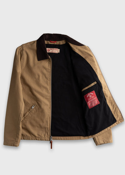 Tan jacket with dark collar, open to show black lining and red label inside. Zippered front and pocket detail visible.