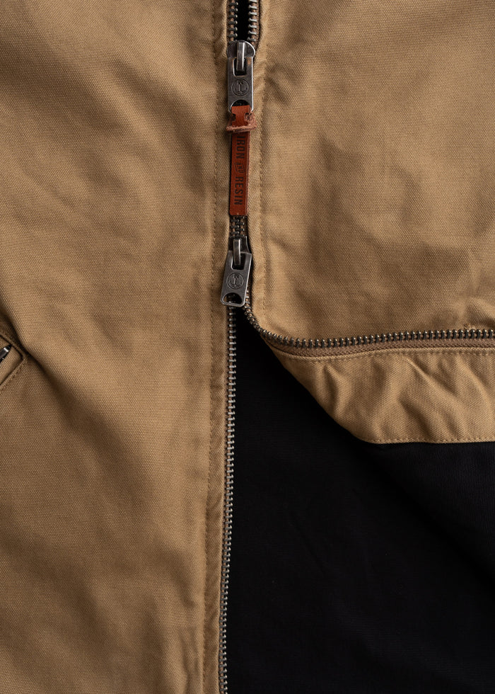Close-up of a brown jacket's metal zipper with a leather pull tab, partially open to reveal a black interior lining.