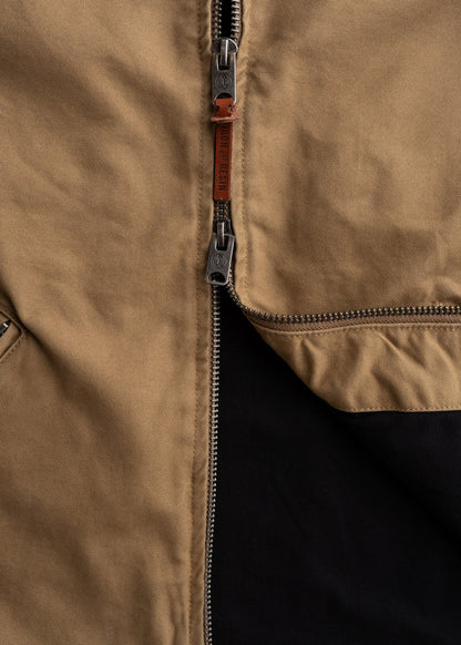 Close-up of a brown jacket's metal zipper with a leather pull tab, partially open to reveal a black interior lining.